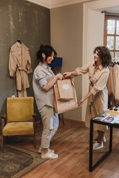 Two women exchanging shopping bags in a stylish boutique, showcasing fashion and smiles.