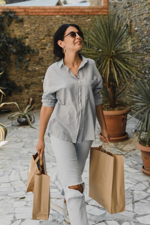 Free Stylish woman with sunglasses carrying shopping bags in sunny outdoor setting. Stock Photo