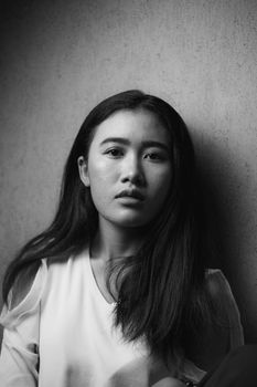 Monochrome portrait of a young woman with long hair against a wall.