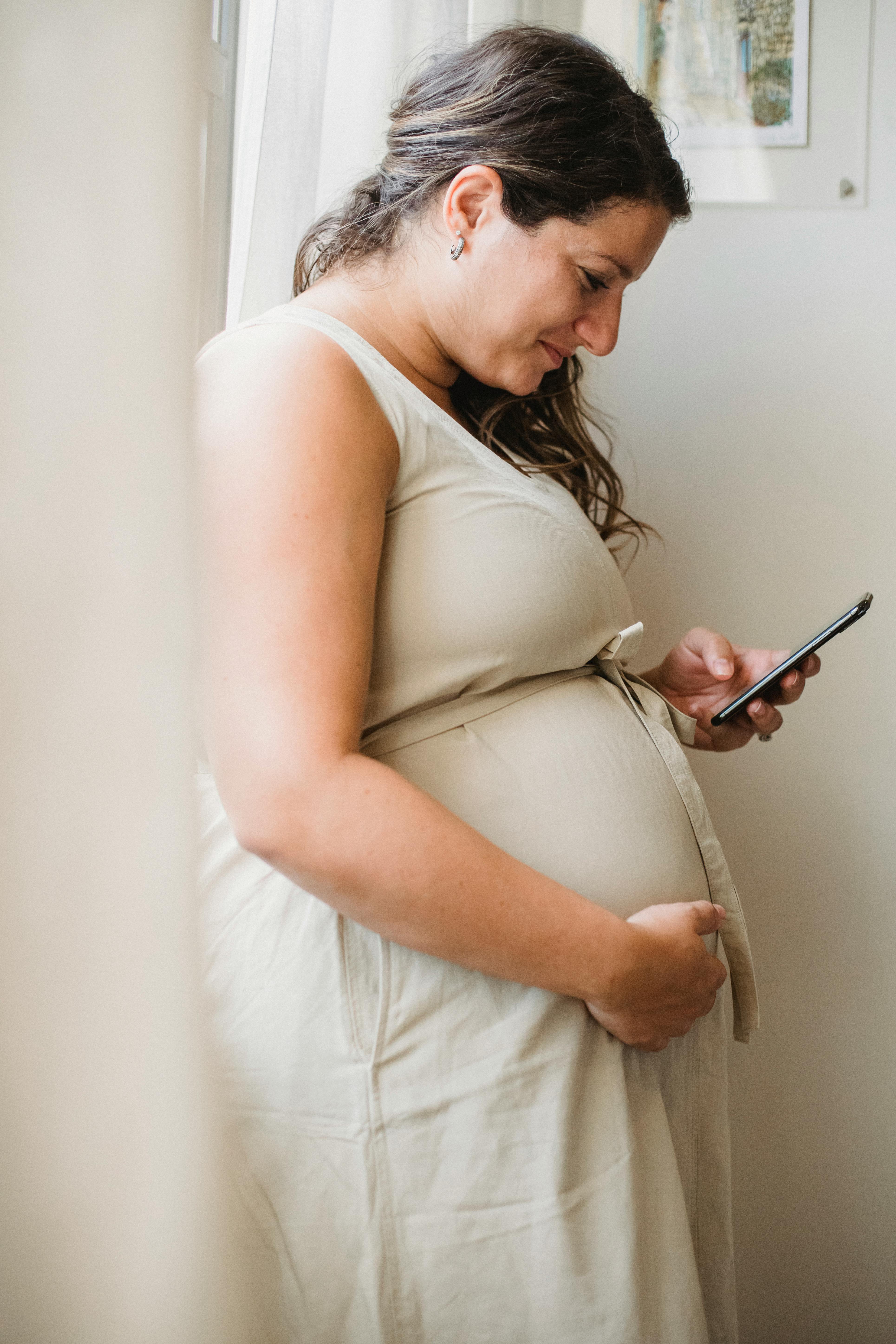 pregnant woman checking notification on smartphone while standing