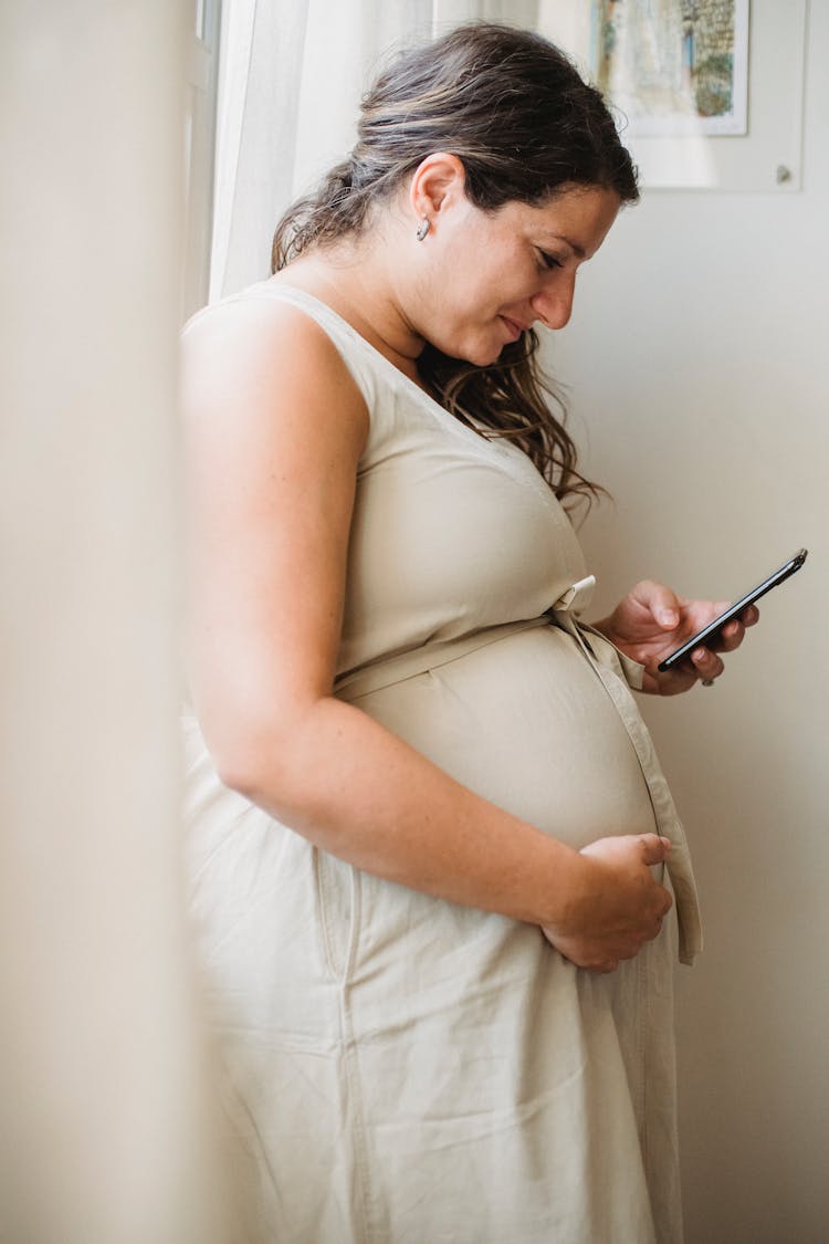 Pregnant Woman Checking Notification On Smartphone While Standing