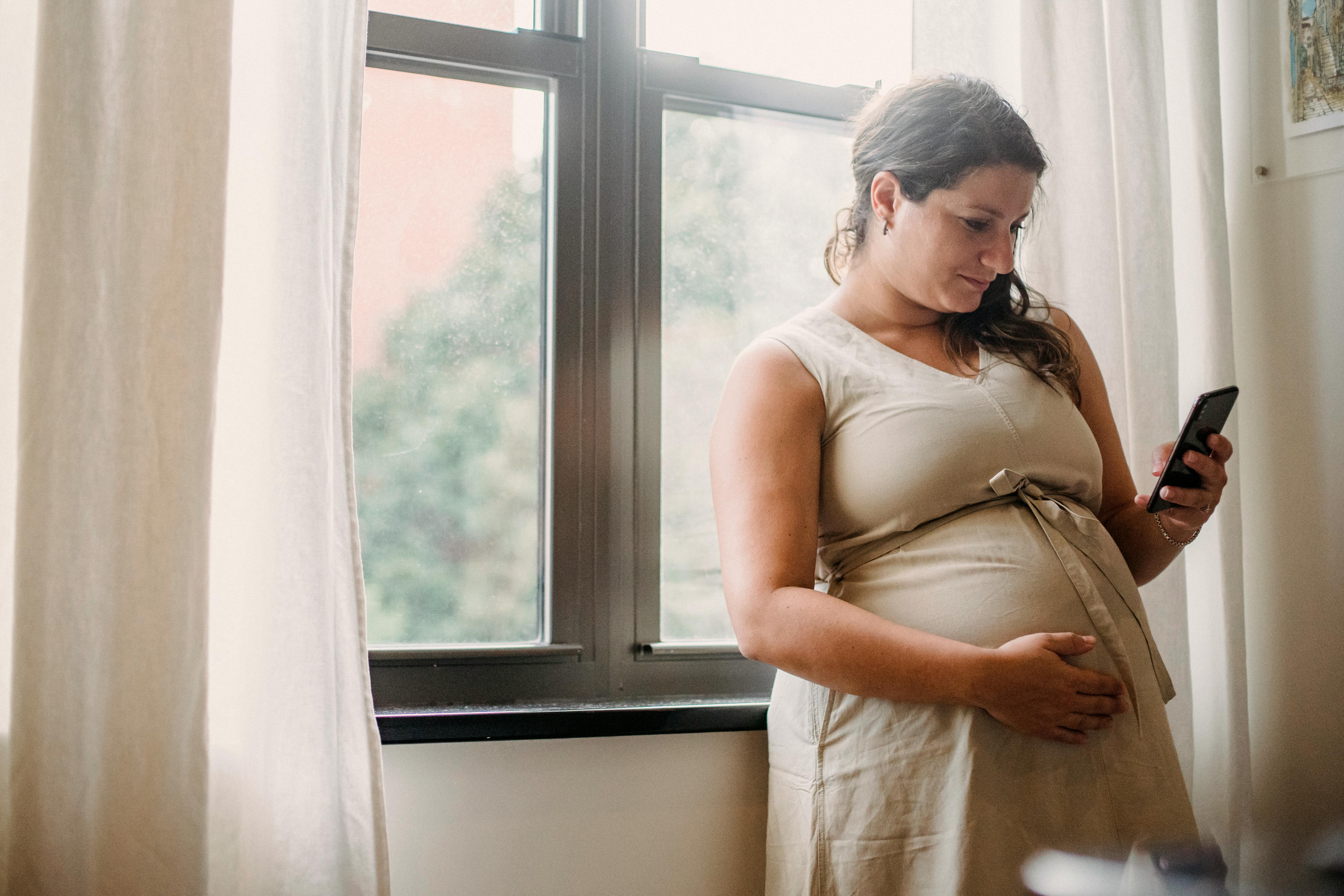 pregnant woman using cellphone while standing at home