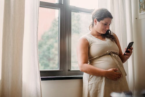 Zwangere Vrouw Met Behulp Van Mobiele Telefoon Terwijl Thuis