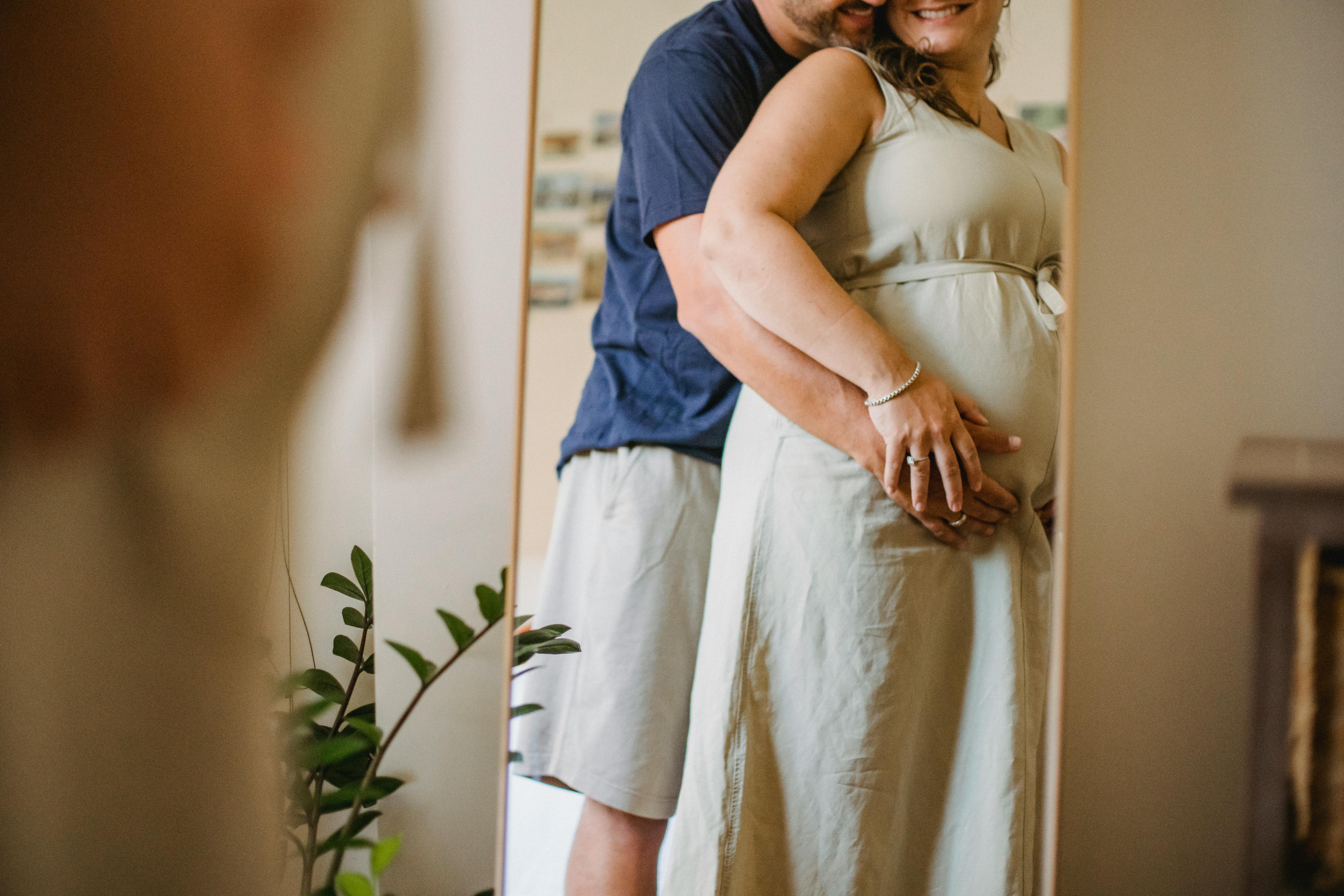 faceless man hugging pregnant woman in light bedroom