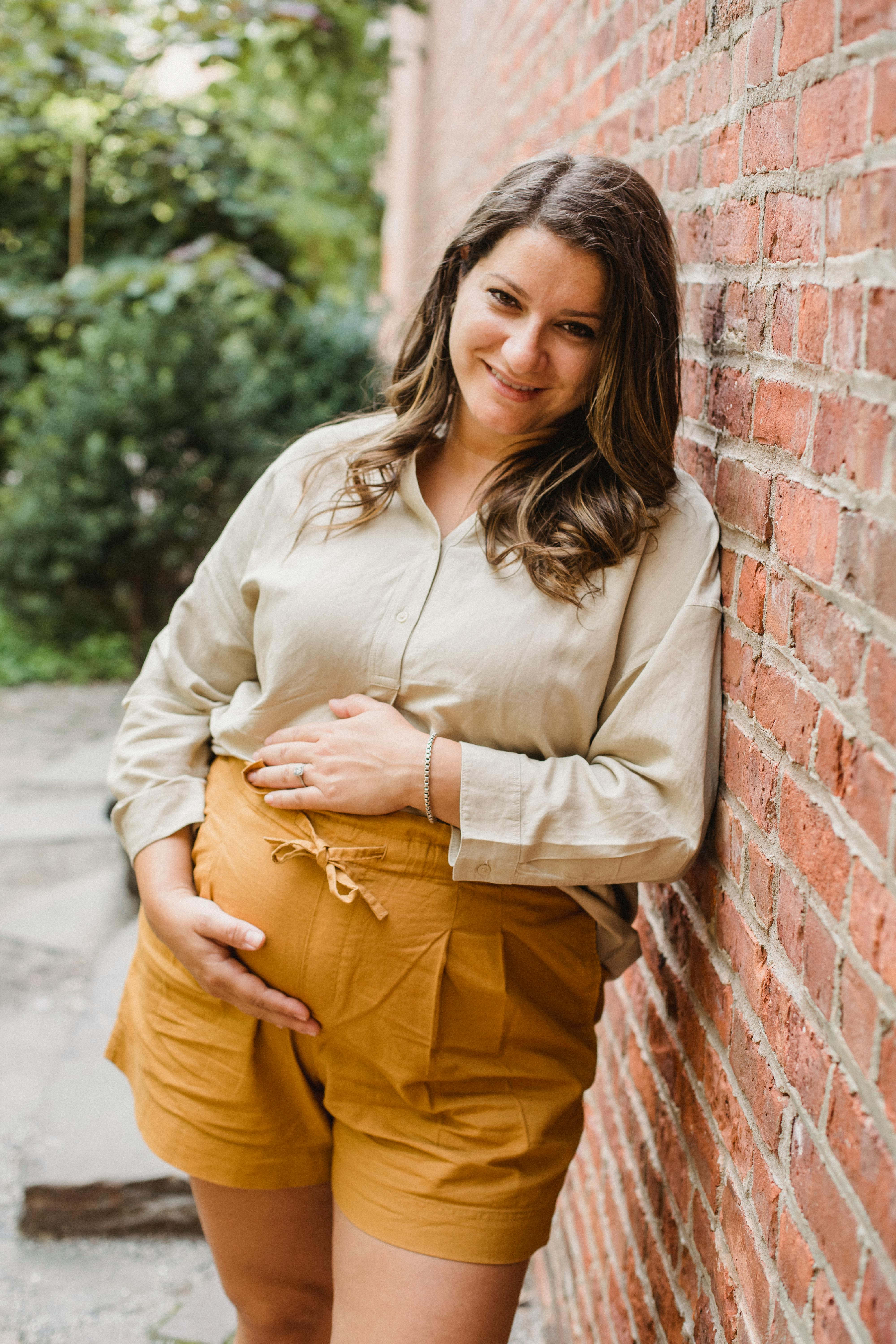 happy pregnant woman leaning on wall in street