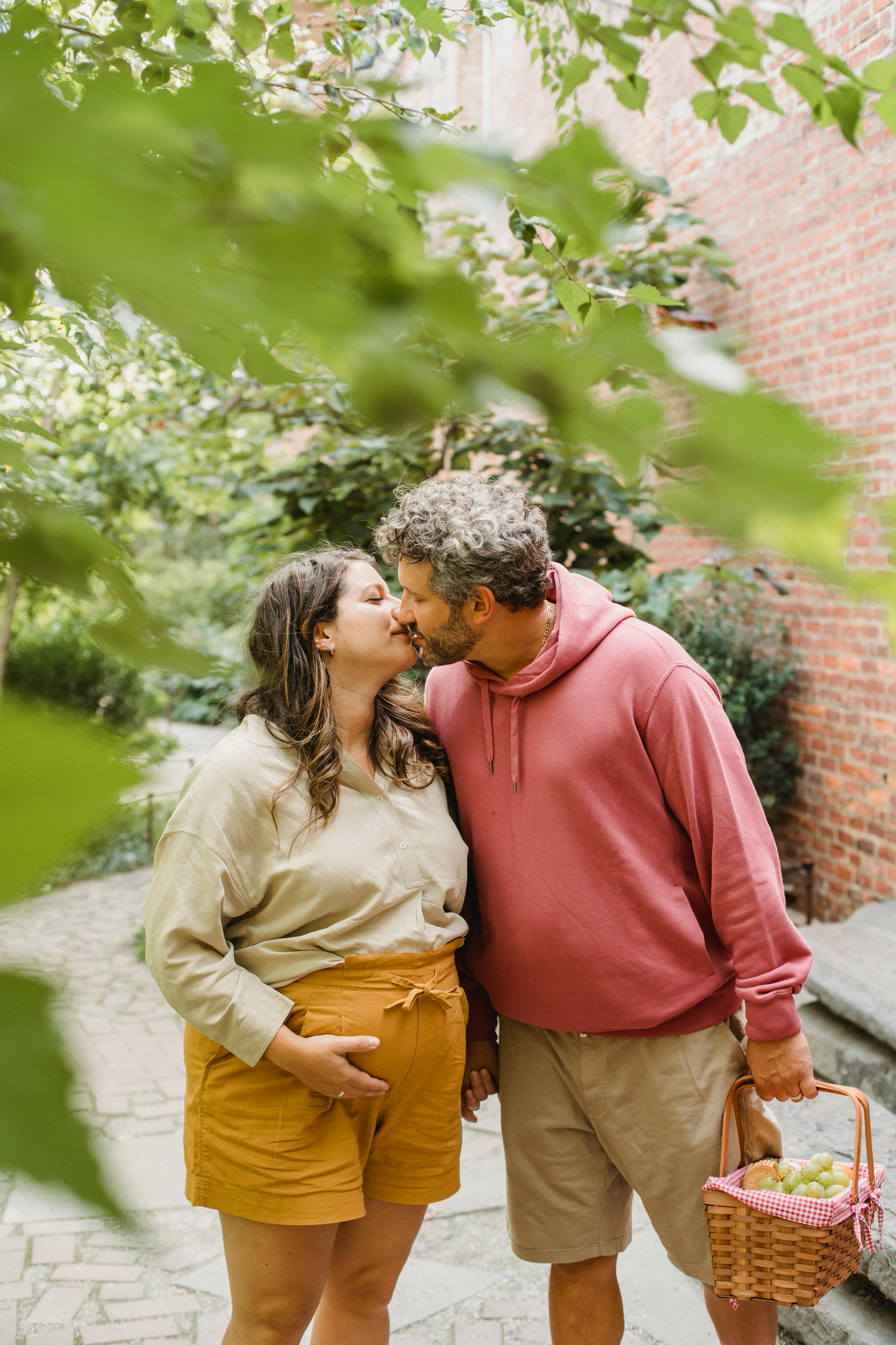 loving pregnant couple with picnic basket kissing in garden