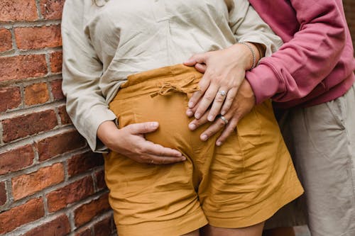 Crop couple in expectancy near brick wall