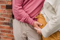 Crop anonymous pregnant female holding hands with husband while hugging near brick wall