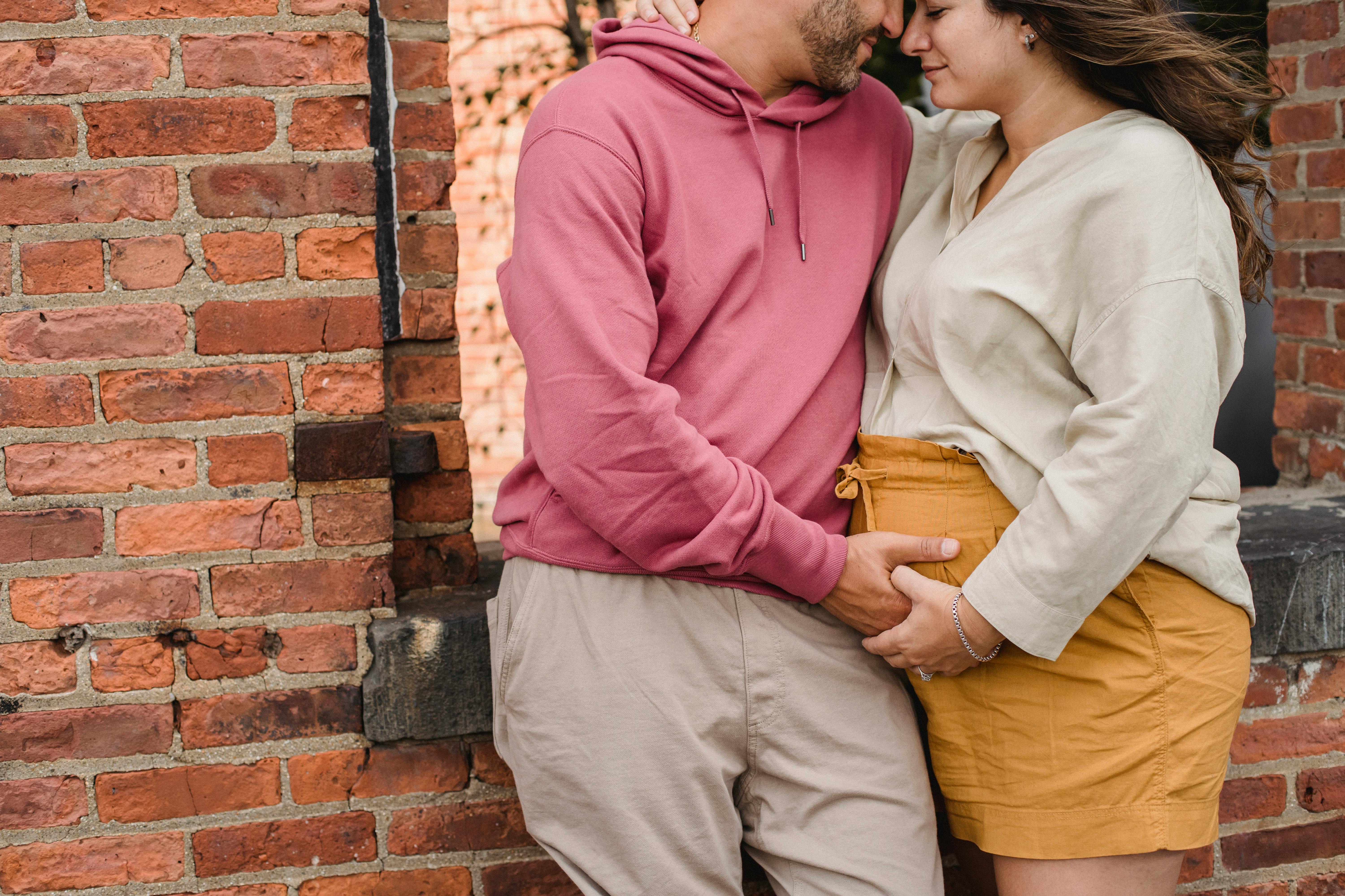 crop couple in expectancy hugging near wall