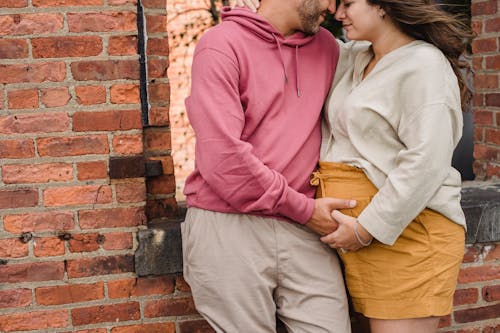 Crop couple in expectancy hugging near wall