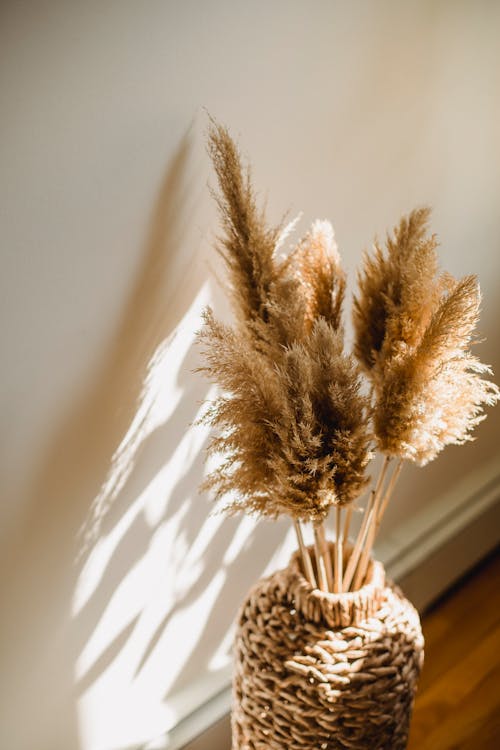 High angle of wicker vase with dried brown plants on floor in room