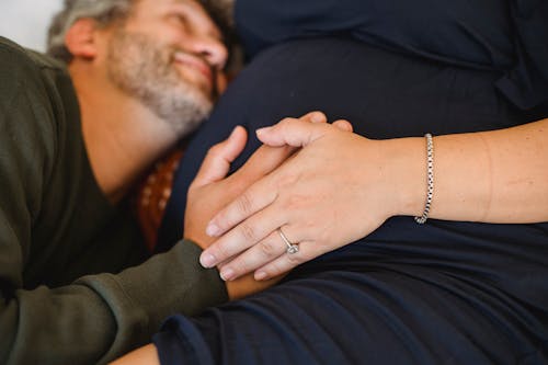Smiling man touching belly of anonymous pregnant wife at home