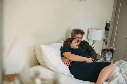 Husband embracing pregnant wife with smartphone on cozy bed