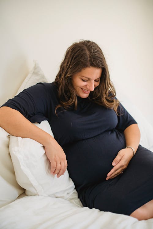 Gratis Sonriente Mujer Embarazada Acariciando La Barriga En La Cama Blanda Foto de stock