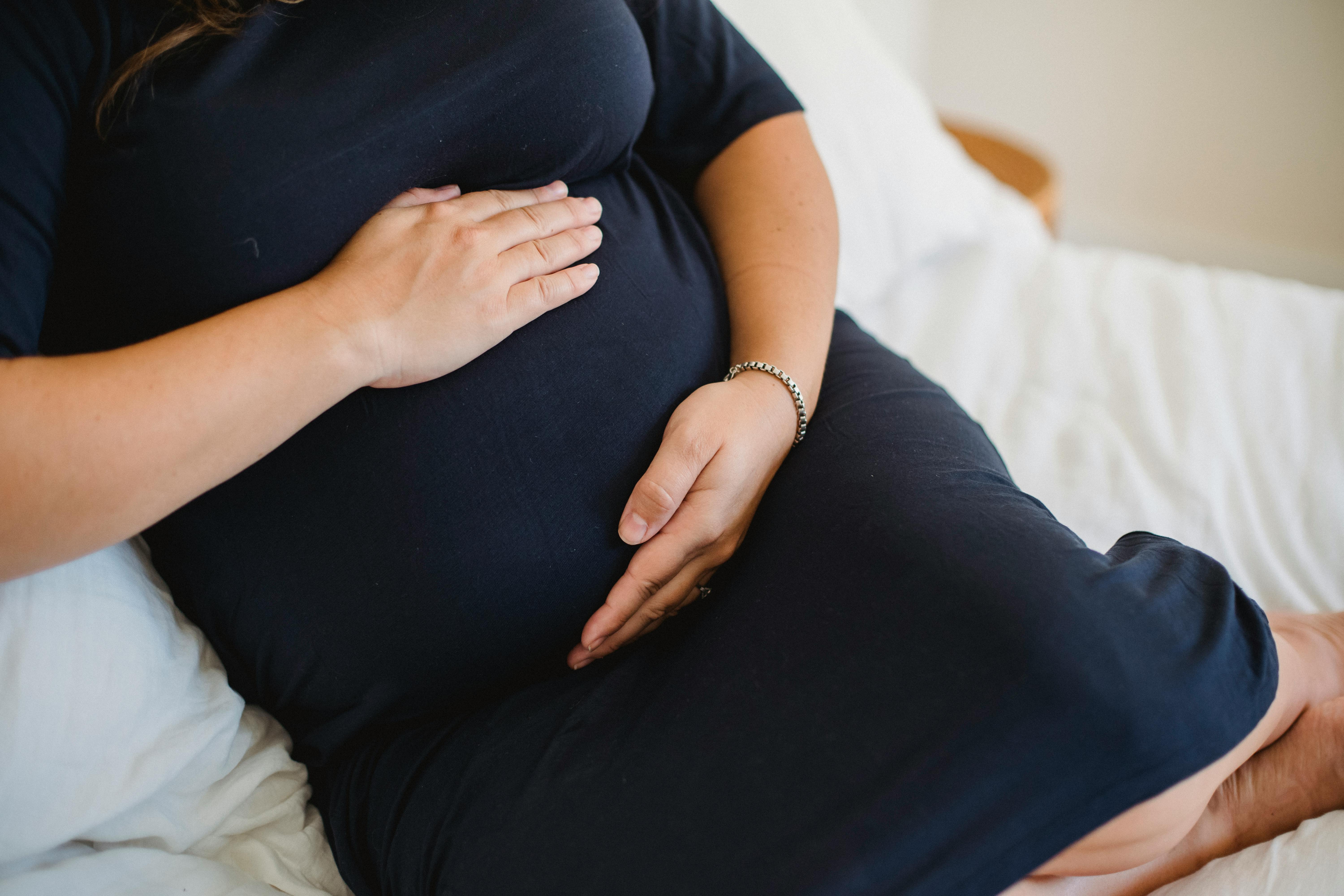 faceless pregnant woman caressing belly on bed at home