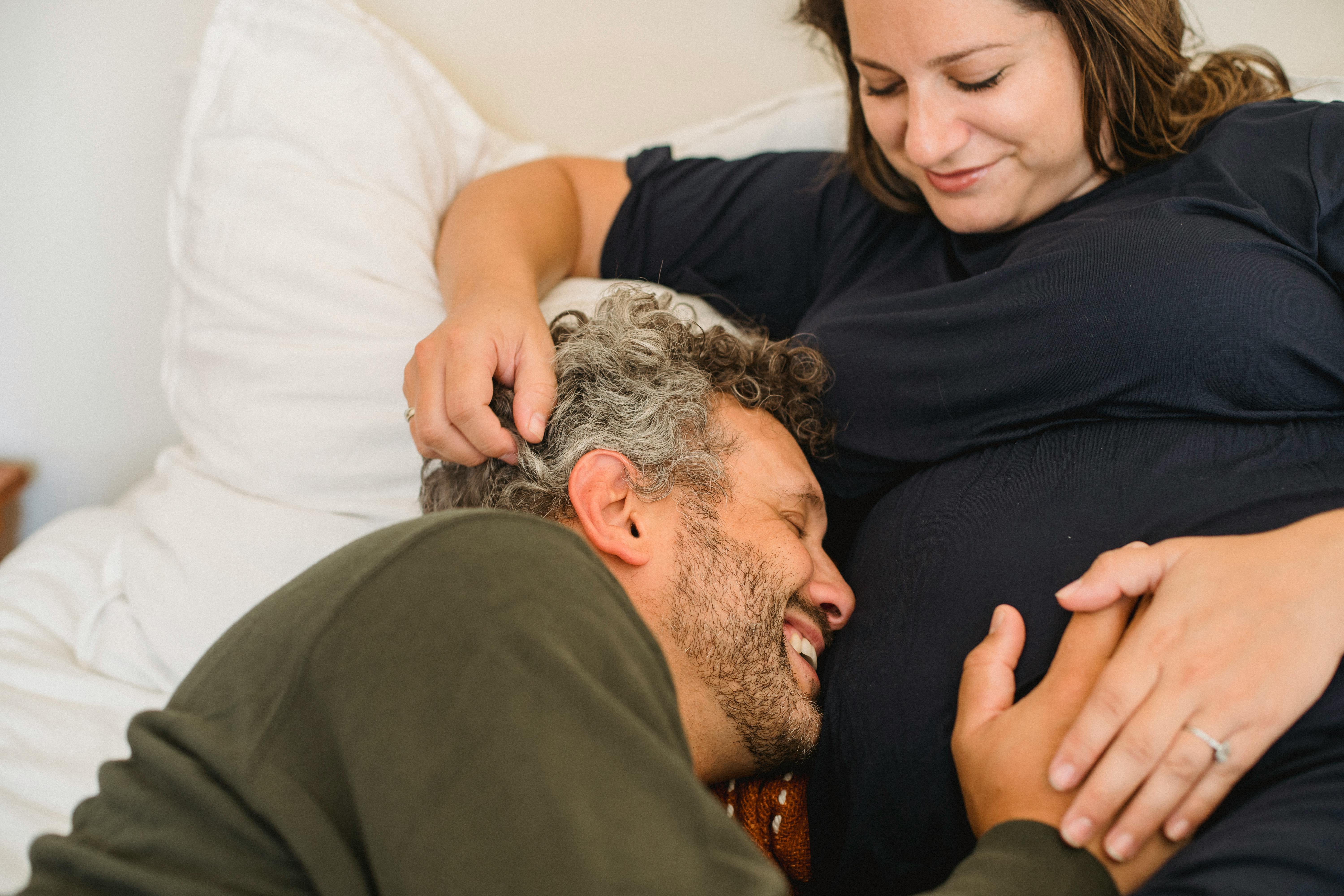 cheerful man caressing tummy of crop pregnant wife on bed