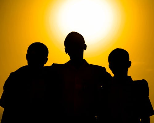 Silhouettes of faceless people hugging while standing against bright orange sky at sundown