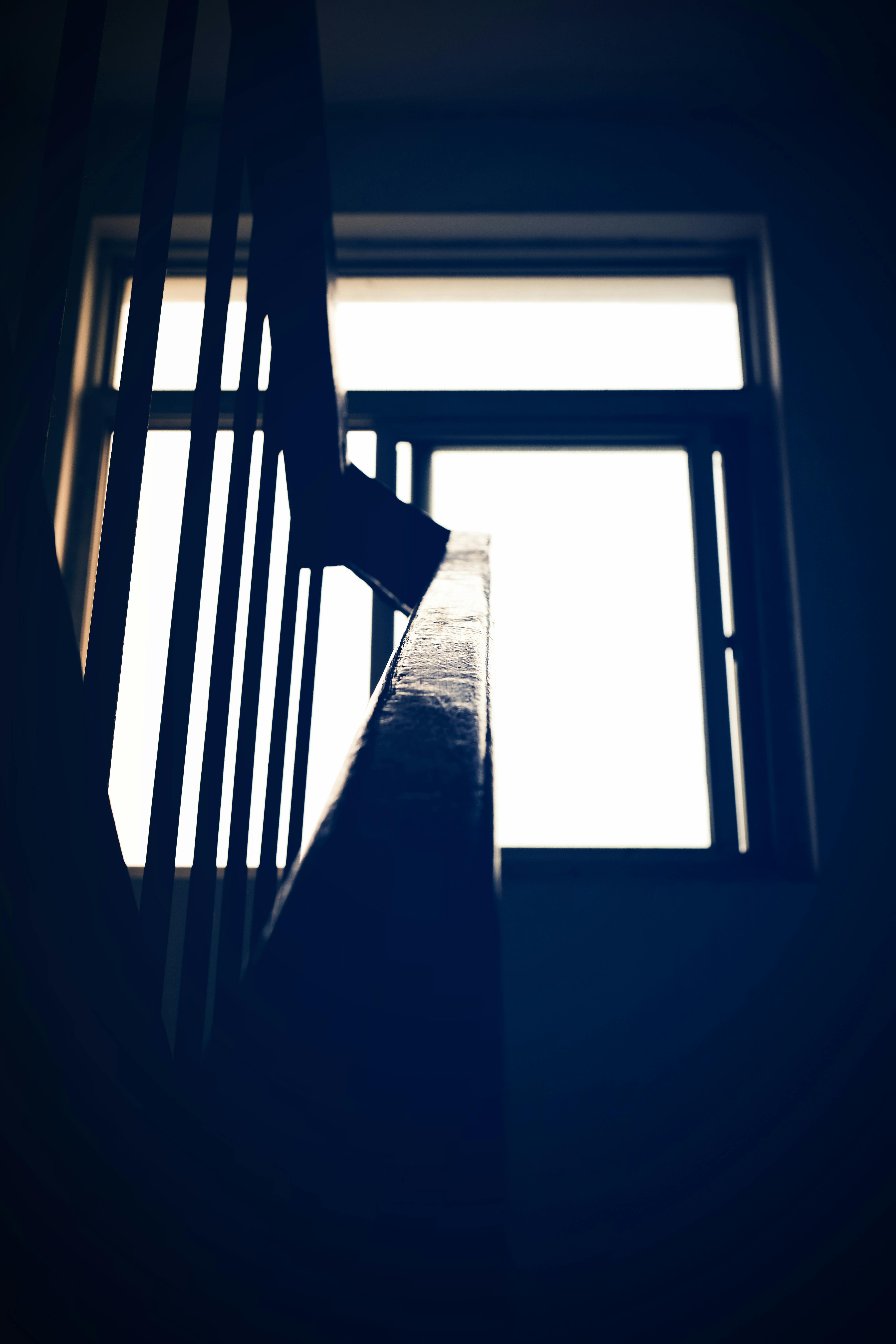 Moody silhouette of a staircase railing with a backlit window indoors, creating dramatic lighting.
