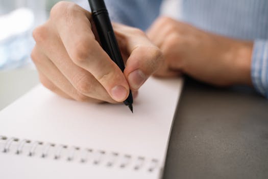 Detailed image of a hand writing with a pen on a spiral notebook, focusing on daily tasks.