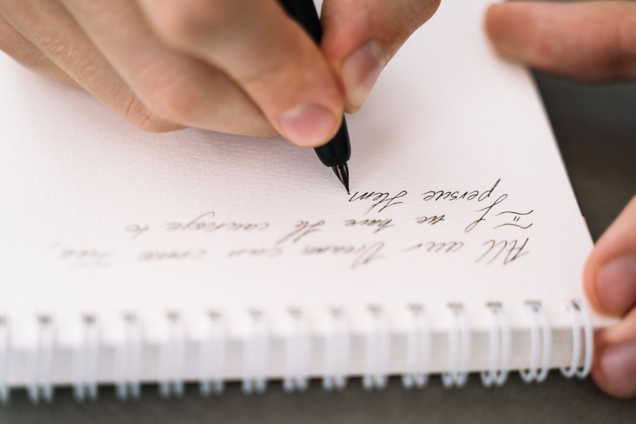A person writing in a spiral notebook with elegant handwriting — practicing letter writing