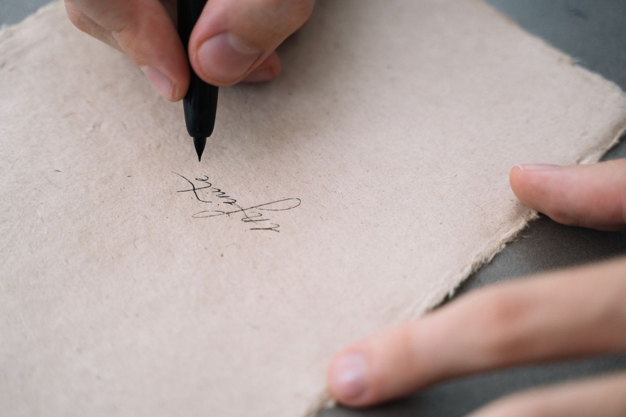 Close-up of a hand writing calligraphy on handmade textured paper — quality handwritten letter