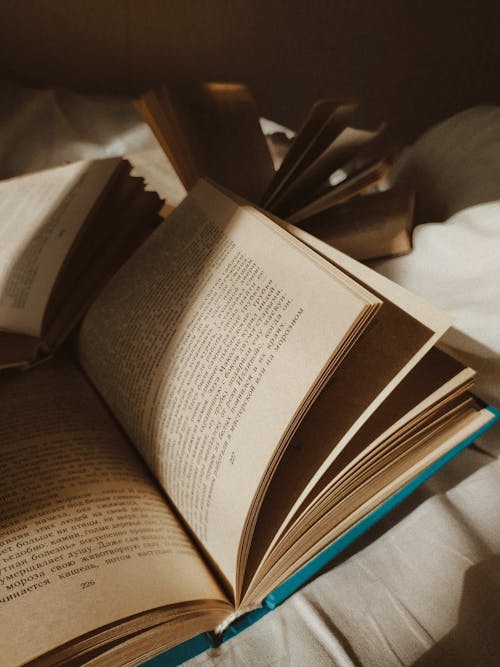 High angle opened books with hardcover placed on white cozy bed in daylight