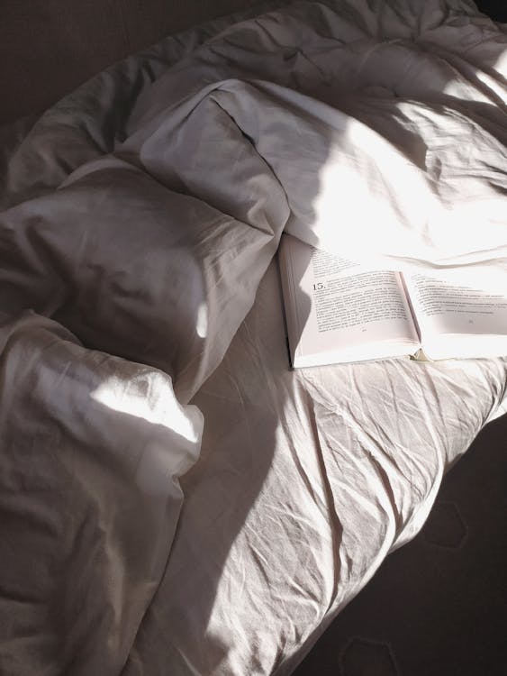 Free Bed with disheveled sheets and opened book Stock Photo