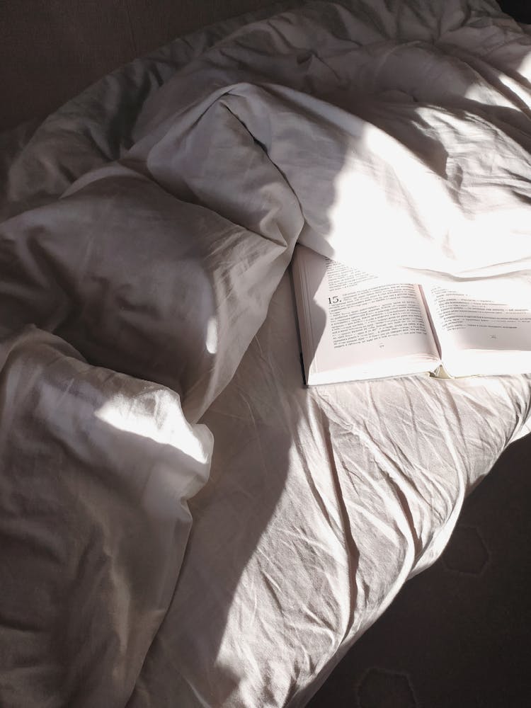 Bed With Disheveled Sheets And Opened Book