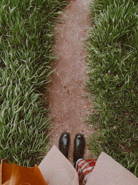 Top view crop unrecognizable female in stylish outfit standing on narrow footpath between grassy lawns