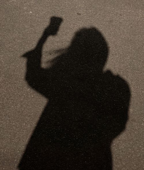 Free A shadow of a person holding an object on pavement seen in sunlight, conveying mystery. Stock Photo