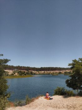 Back view anonymous person sunbathing on sandy lake coast on sunny summer weather