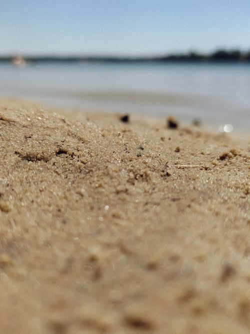 Free Macro shot of sandy beach with blurred water in the background, creating a serene atmosphere. Stock Photo