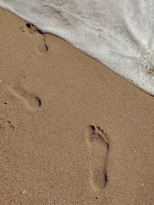 Top view barefoot human footprints left on sandy seacoast washed by foamy seawater