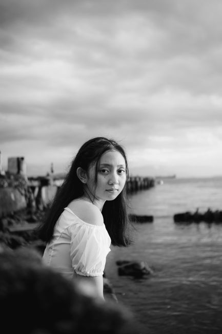 Black and white side view of attentive ethnic female adolescent in trendy wear looking at camera near river with stones