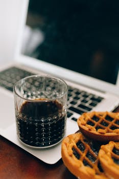 A cozy setup with coffee and waffles beside a laptop, perfect for work or leisure.