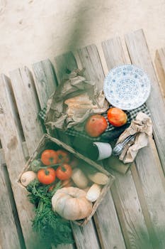 Aerial view of fresh vegetables, bread, and rustic tableware outdoors on a wooden table.