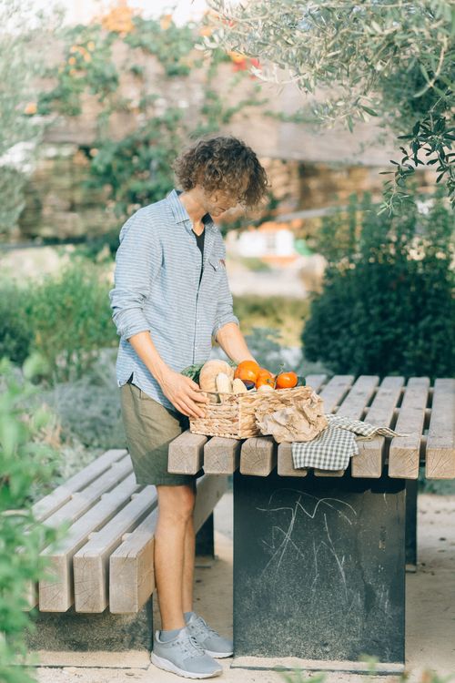 Free Person arranging fresh vegetables in a basket on a table in a garden setting. Stock Photo