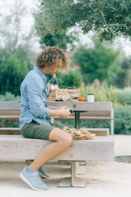 Free Casual young man sitting on a bench in a garden, enjoying a healthy meal on a summer day. Stock Photo