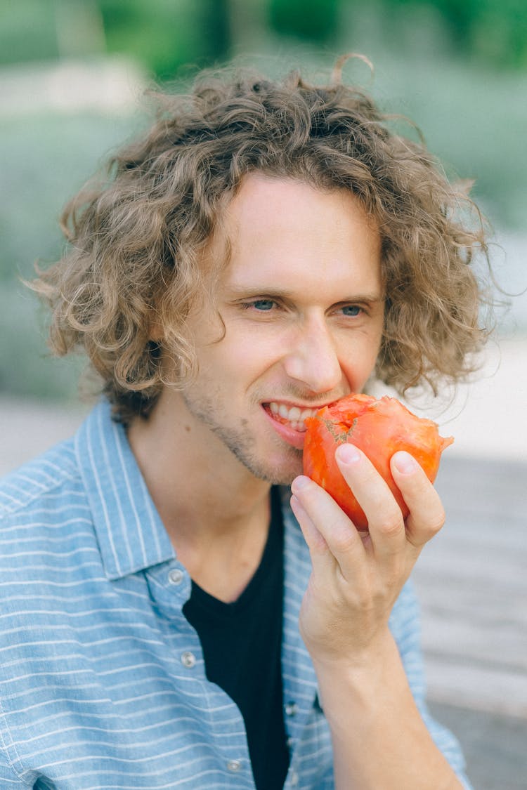 A Man In Striped Polo Shirt Eating Tomato