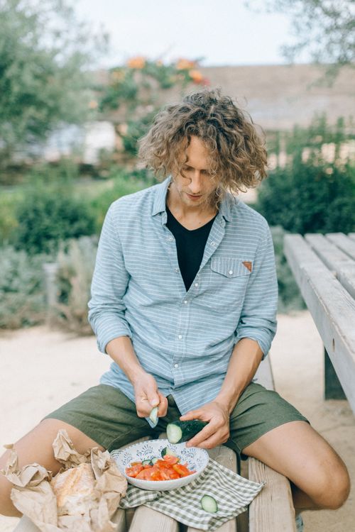 Free Young man slicing vegetables for a fresh salad sitting outdoors in a garden setting. Stock Photo
