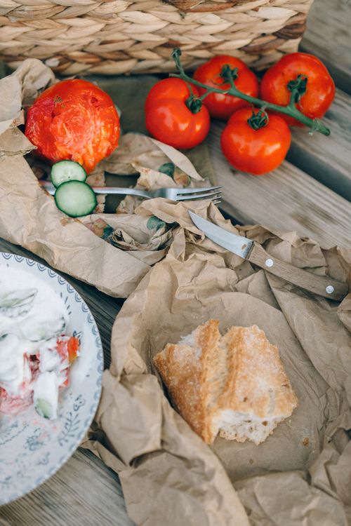 Free A rustic outdoor picnic with fresh tomatoes, bread, and cucumber slices on a wooden table. Stock Photo