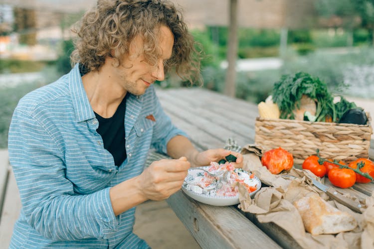 Man Eating Vegetable Salad At A Picnic Table