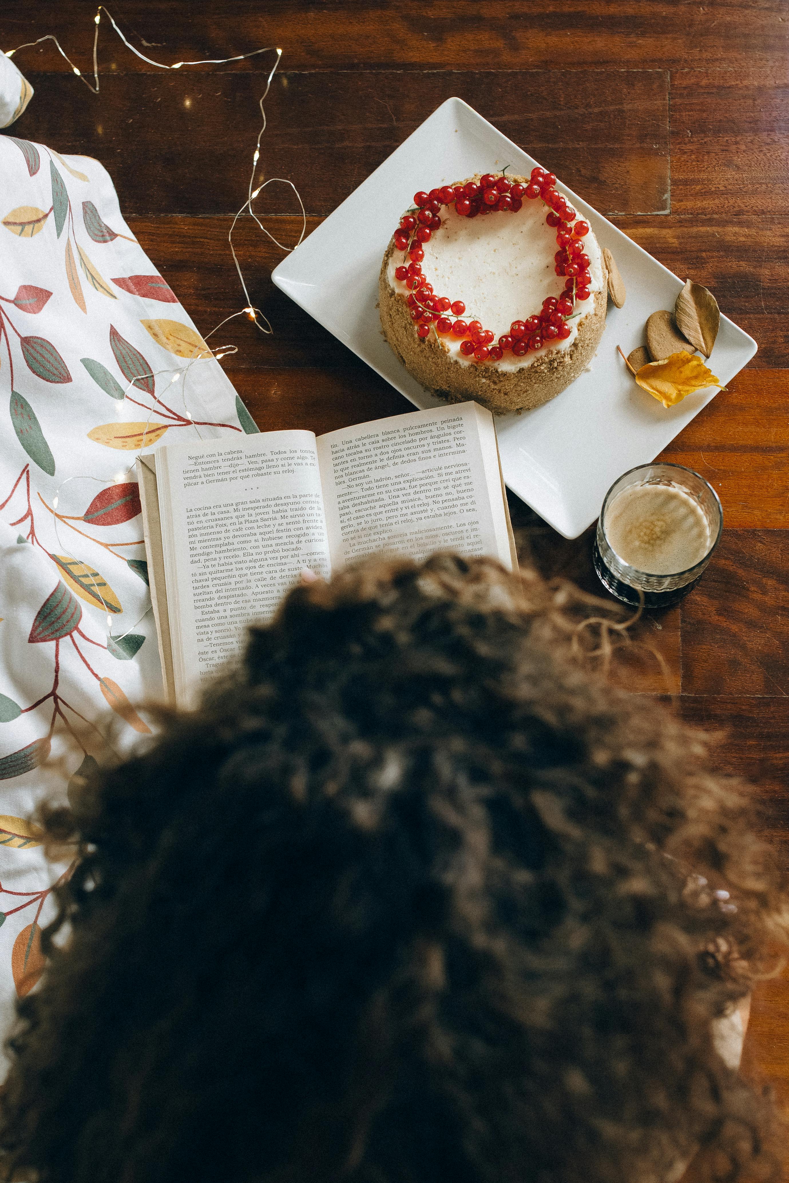 Free A person enjoys reading near a cozy setting with cake and coffee on a wooden surface. Stock Photo