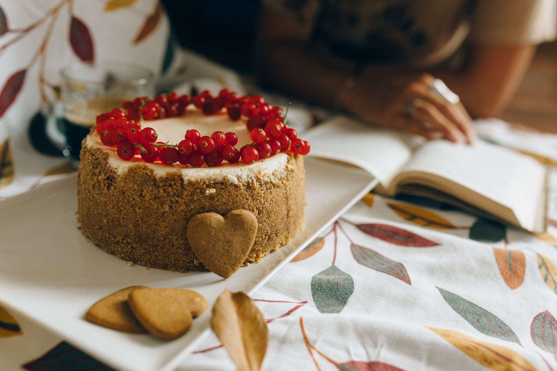 A tempting cake adorned with lingonberries and heart-shaped cookies on a leaf-patterned tablecloth.