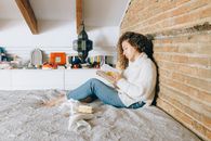 Woman in White Sweater and Blue Denim Jeans Sitting on White and Brown Floral Area Rug