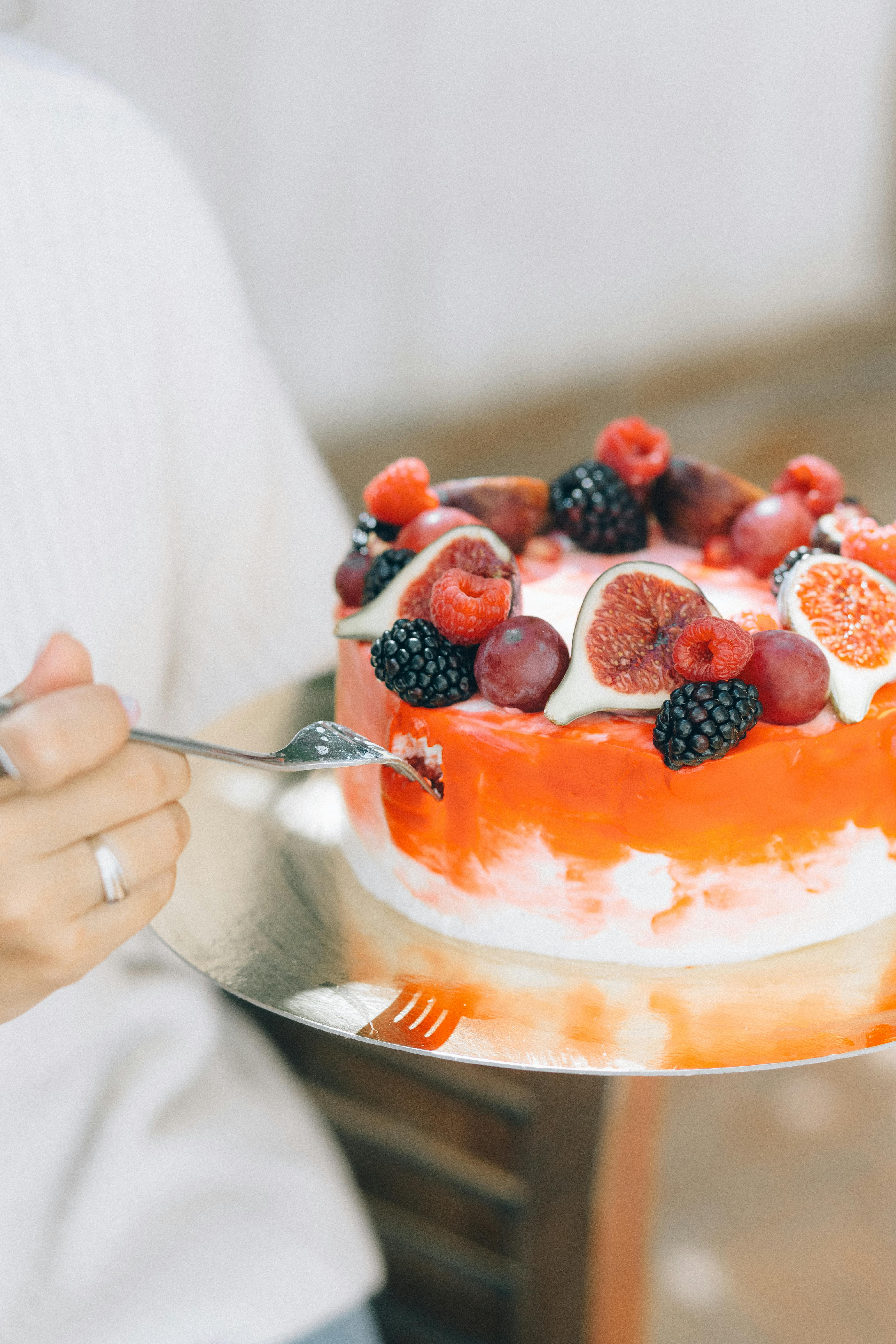 person holding stainless steel spoon with sliced strawberries and blueberries