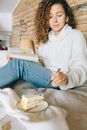 Woman in White Sweater and Blue Denim Jeans Sitting on White Textile