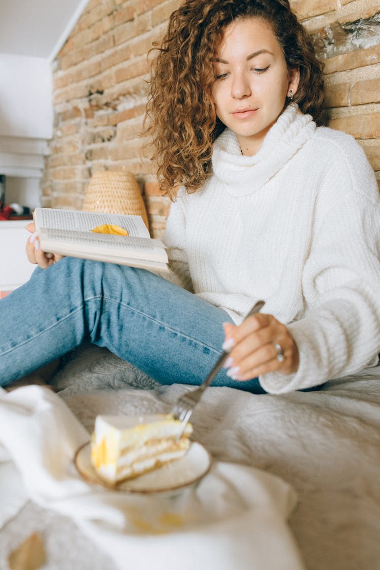 A Woman Eating Cake While Reading A Book