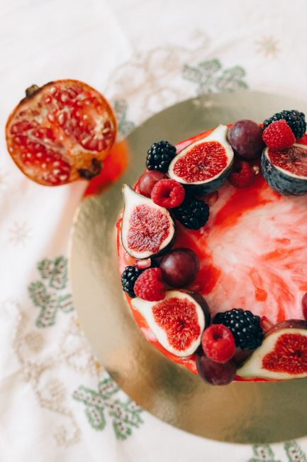 Overhead view of a delectable fruit cake topped with figs, berries, and a touch of pomegranate.