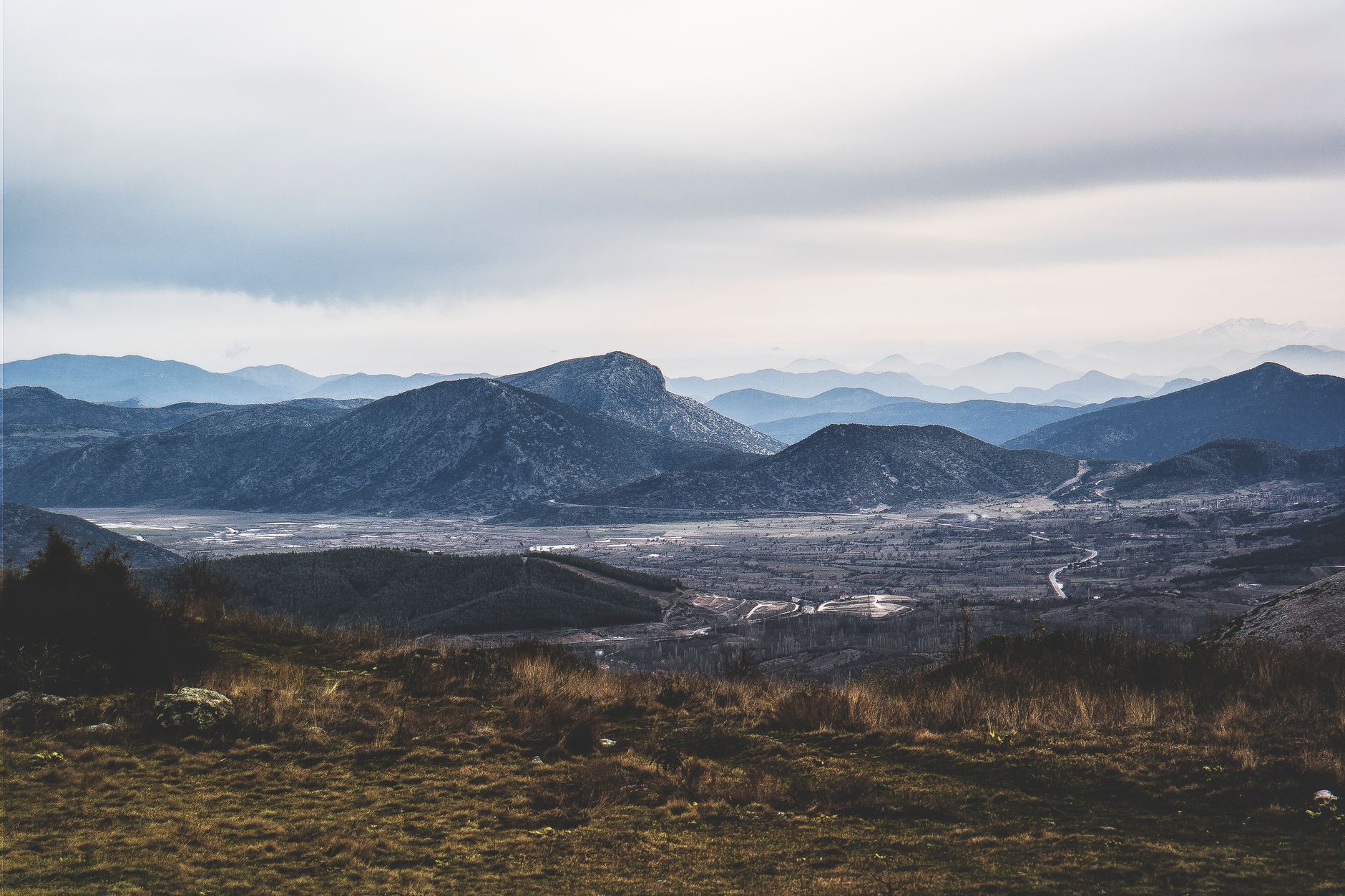 A beautiful view of hilly grasslands extending to distant mountains under a cloudy sky.